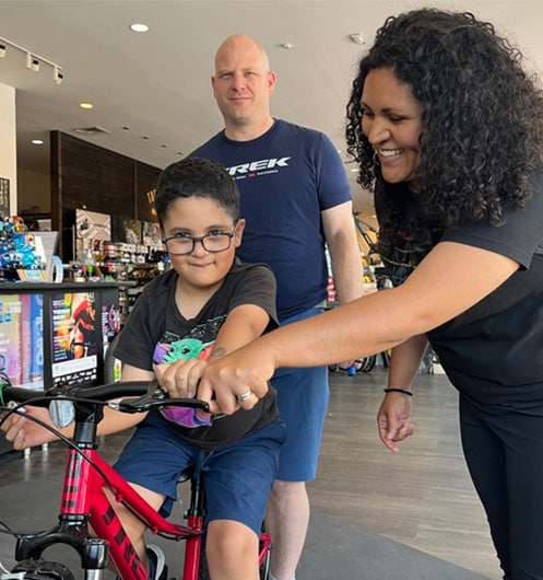Boy on red bike with mother holding handle after winning bike at Child in the Wild
