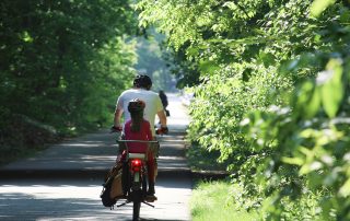 Photo of man with his daugther on the back of his bike riding along beautiful greenway