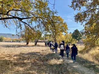 A group of people walking along a dirt trail on the Southeast Greenway under autumn trees with yellow leaves.